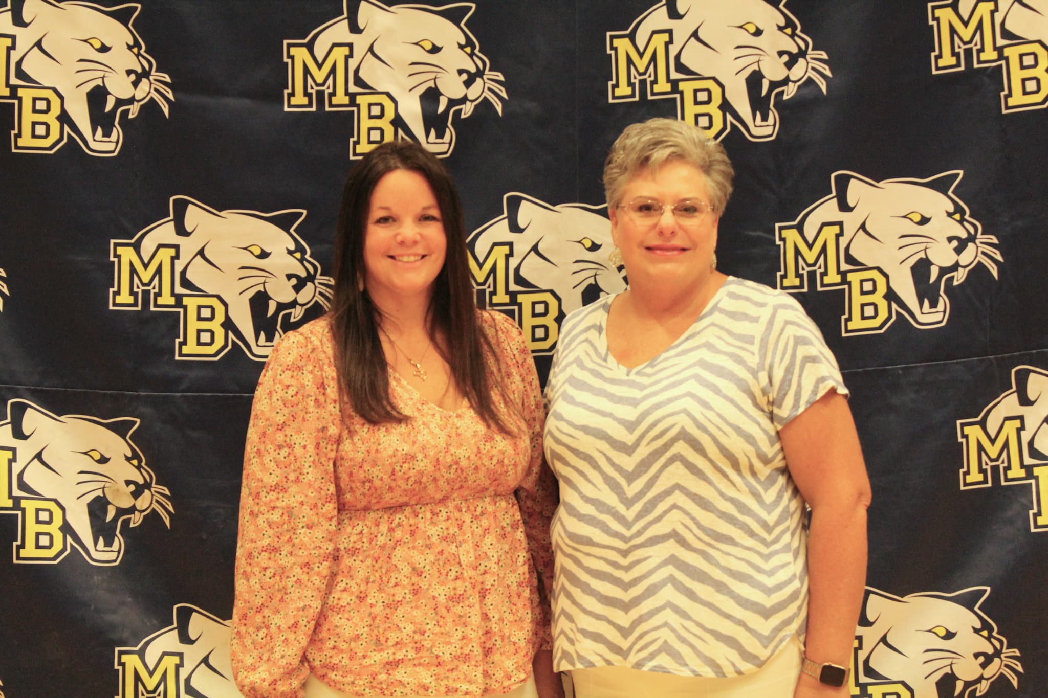 Two women pose in front of a Mt. Blue backdrop